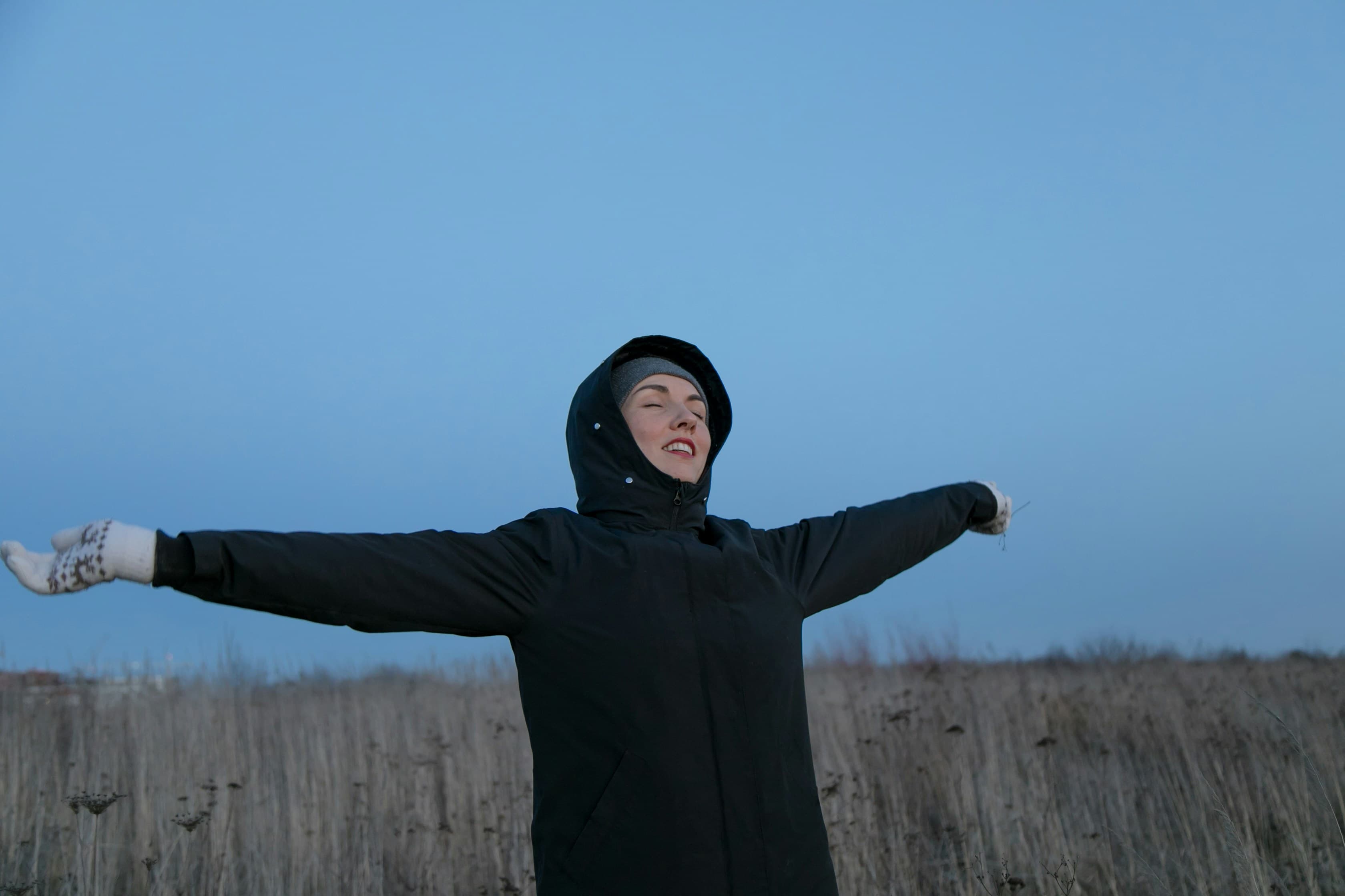 A person standing in an open field with arms outstretched, conveying freedom and relief